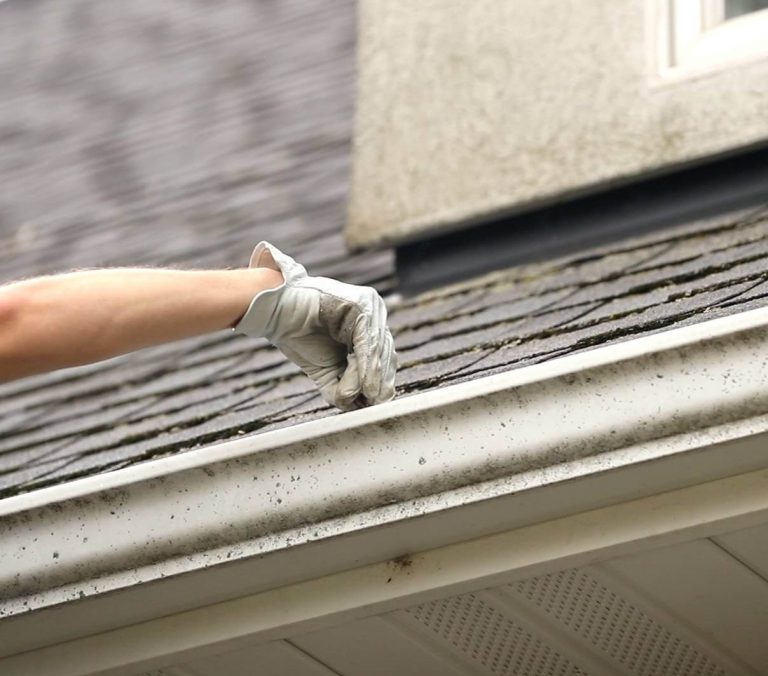 Closeup of a gloved hand cleaning a gutter